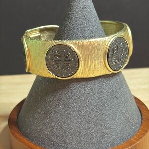 Textured gold tone hinged cuff bracelet with deep gray holy emblems